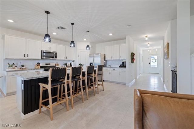 kitchen with hanging light fixtures, white cabinetry, appliances with stainless steel finishes, and a kitchen island with sink