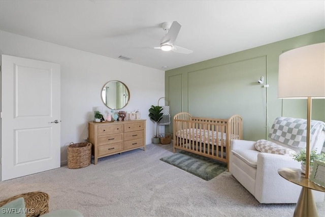 bedroom with a nursery area, light colored carpet, and ceiling fan