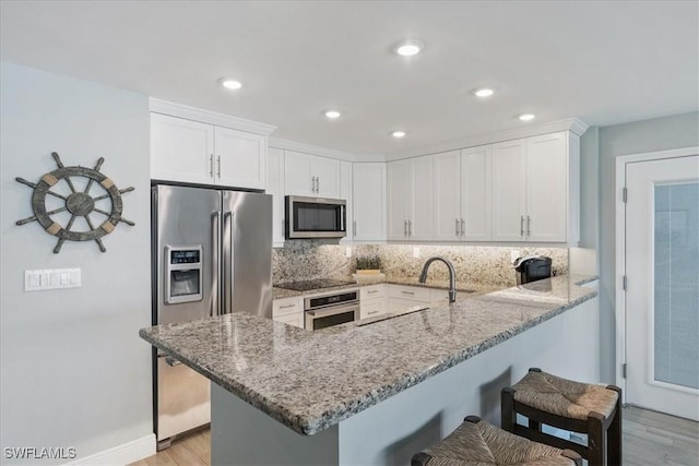 kitchen featuring appliances with stainless steel finishes, white cabinetry, backsplash, light stone counters, and kitchen peninsula