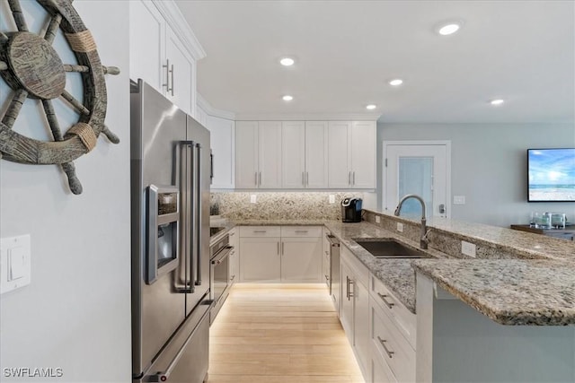 kitchen featuring stainless steel appliances, kitchen peninsula, sink, and white cabinets