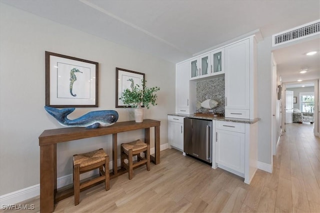 bar featuring light stone countertops, fridge, white cabinets, and light hardwood / wood-style flooring