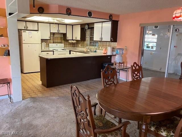 kitchen with a textured ceiling, kitchen peninsula, white cabinets, white appliances, and backsplash