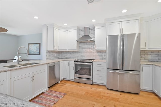 kitchen featuring wall chimney exhaust hood, sink, light wood-type flooring, appliances with stainless steel finishes, and white cabinets