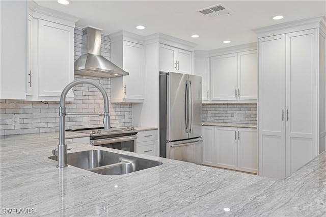 kitchen featuring light stone counters, wall chimney range hood, stainless steel fridge, and white cabinets