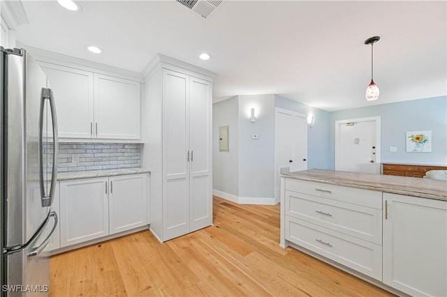 kitchen with stainless steel fridge, light stone countertops, light hardwood / wood-style floors, white cabinets, and decorative light fixtures