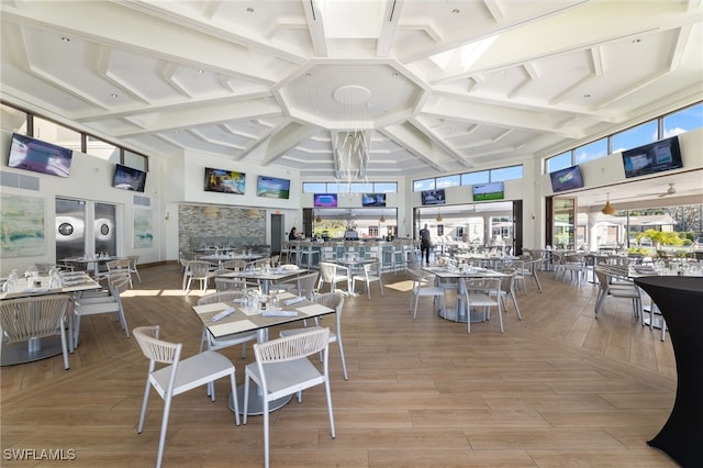 dining room featuring coffered ceiling, a towering ceiling, and light hardwood / wood-style floors