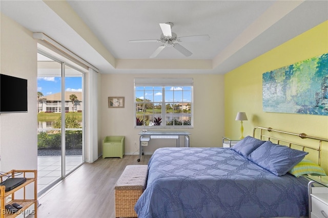 bedroom with ceiling fan, access to outside, light wood-type flooring, and a tray ceiling