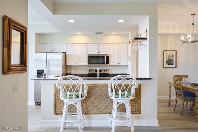 kitchen featuring dark stone countertops, decorative light fixtures, white cabinets, and appliances with stainless steel finishes