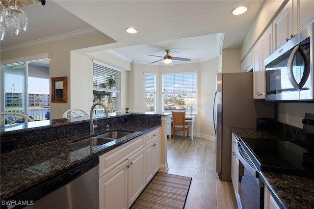 kitchen with sink, appliances with stainless steel finishes, white cabinetry, ornamental molding, and dark stone counters