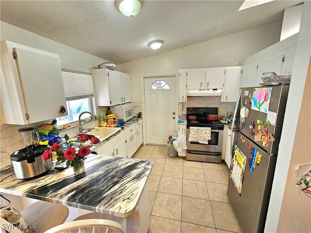 kitchen with sink, white cabinetry, vaulted ceiling, light tile patterned floors, and stainless steel appliances