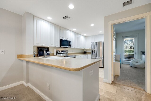 kitchen with sink, appliances with stainless steel finishes, white cabinetry, light colored carpet, and kitchen peninsula