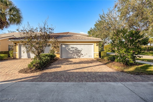 ranch-style home featuring stucco siding, a tiled roof, an attached garage, and decorative driveway