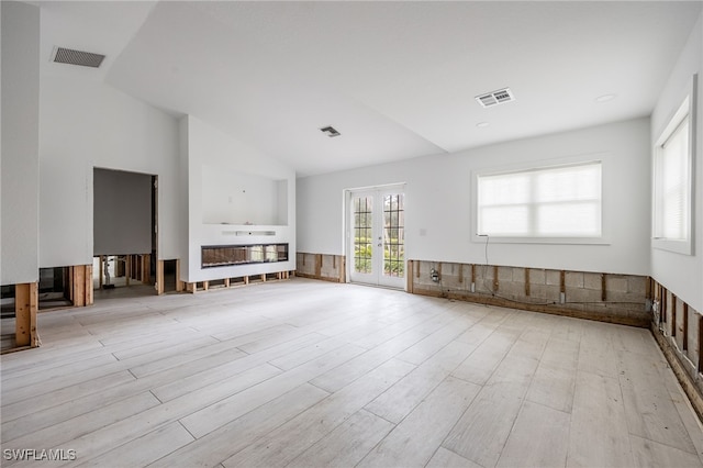 unfurnished living room featuring vaulted ceiling, light hardwood / wood-style floors, and french doors