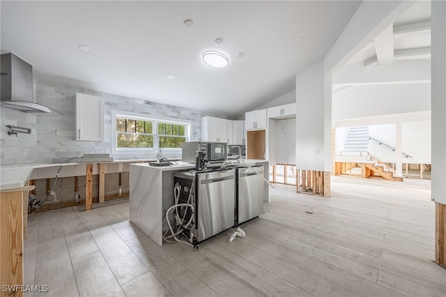 kitchen with white cabinetry, tasteful backsplash, vaulted ceiling, stainless steel dishwasher, and wall chimney range hood