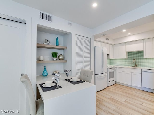 kitchen with sink, white cabinets, decorative backsplash, light hardwood / wood-style floors, and white appliances