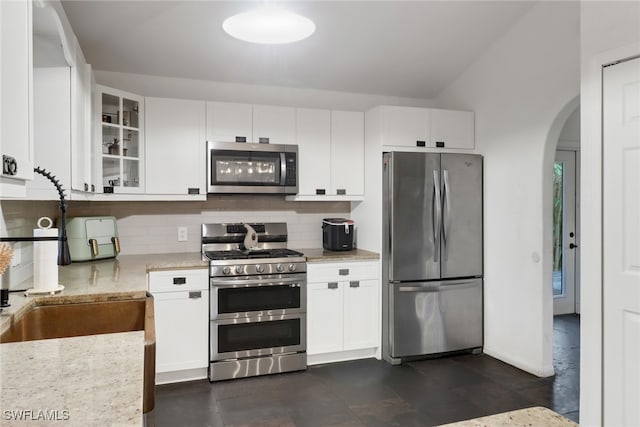 kitchen with vaulted ceiling, appliances with stainless steel finishes, white cabinetry, backsplash, and light stone countertops