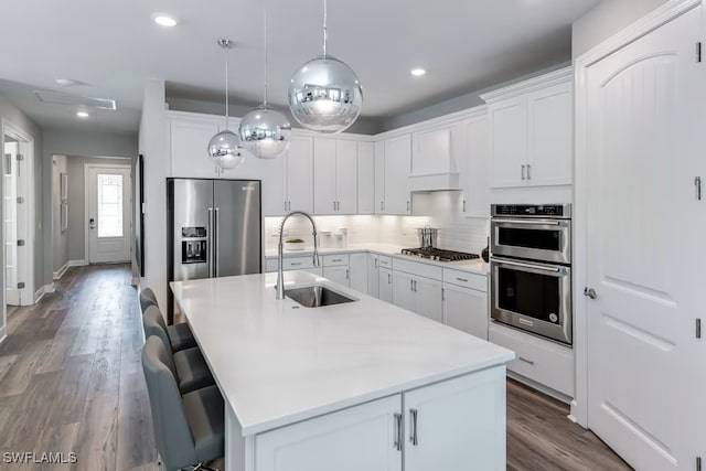 kitchen with stainless steel appliances, white cabinetry, sink, and premium range hood