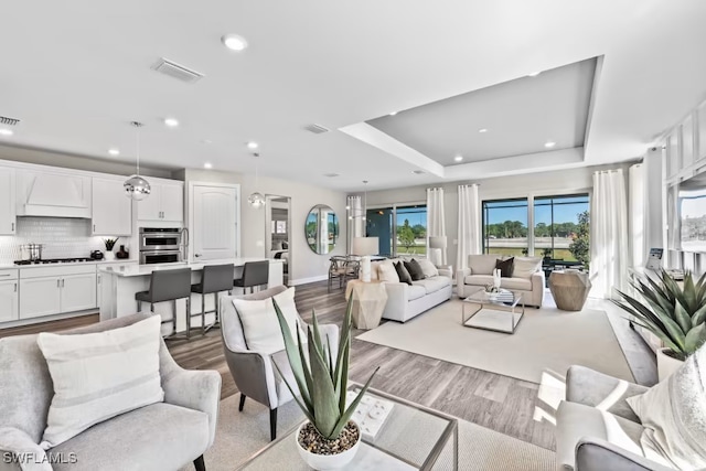 living room with light wood-type flooring and a tray ceiling