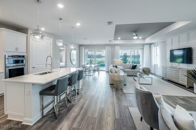 kitchen featuring pendant lighting, sink, white cabinetry, double oven, and a center island with sink