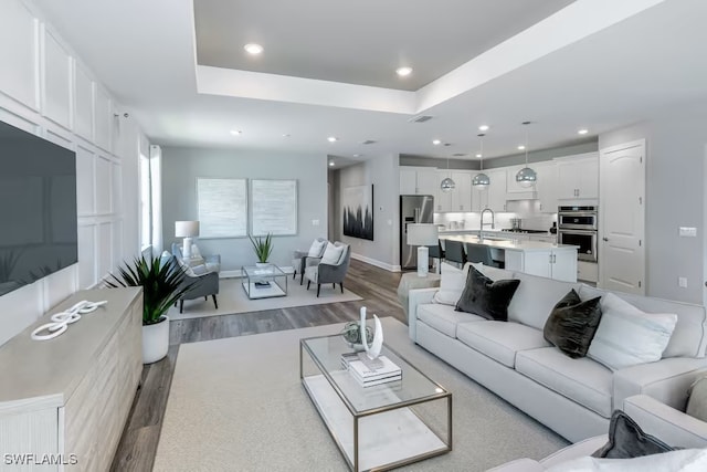 living room with sink, a raised ceiling, and light wood-type flooring