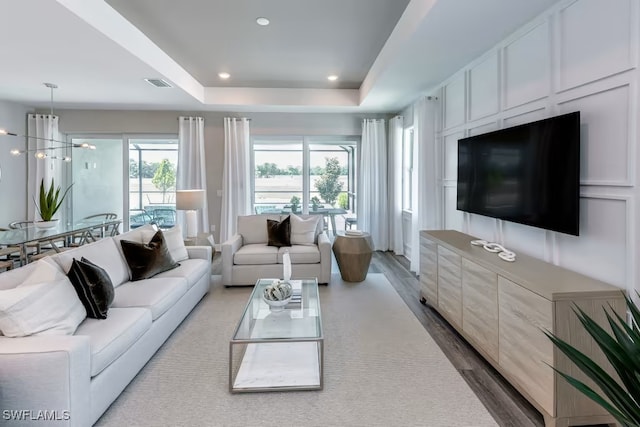 living room with light hardwood / wood-style flooring, a tray ceiling, a wealth of natural light, and a chandelier