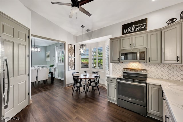 kitchen with vaulted ceiling, appliances with stainless steel finishes, pendant lighting, tasteful backsplash, and dark wood-type flooring