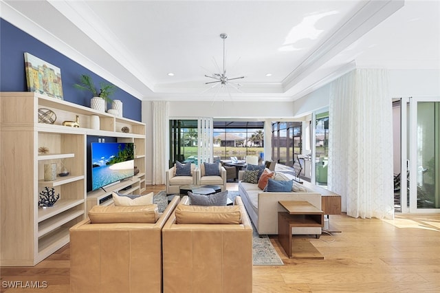 living room with crown molding, a tray ceiling, light hardwood / wood-style floors, and a chandelier