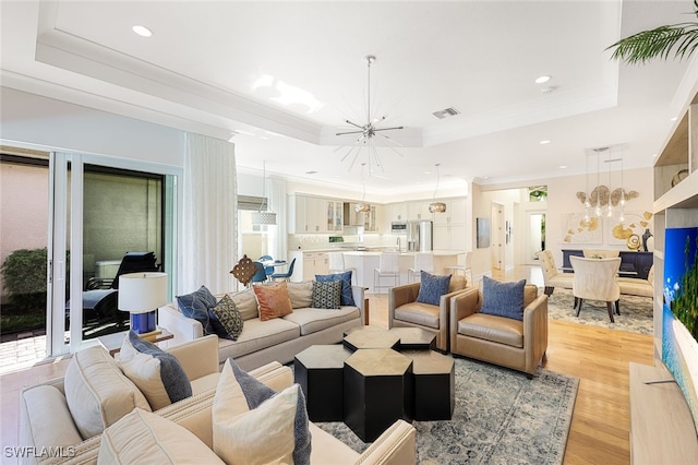 living room with an inviting chandelier, a raised ceiling, and light hardwood / wood-style flooring