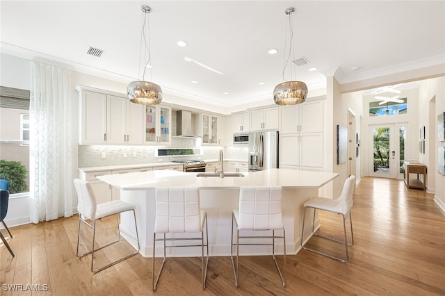 kitchen featuring a large island with sink, appliances with stainless steel finishes, sink, and wall chimney exhaust hood