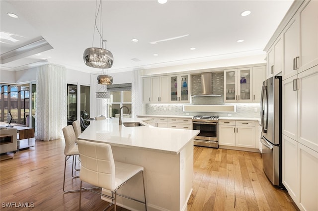 kitchen featuring appliances with stainless steel finishes, sink, a breakfast bar area, a kitchen island with sink, and wall chimney exhaust hood