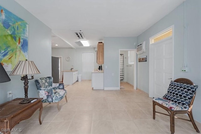 living area featuring light tile patterned flooring, a wall unit AC, and baseboards