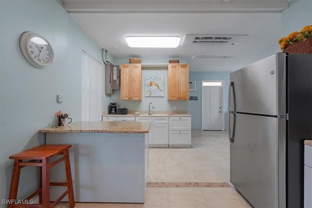 kitchen with visible vents, a breakfast bar area, freestanding refrigerator, light brown cabinets, and a sink