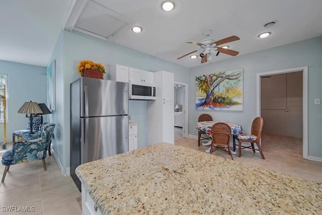 kitchen with light stone counters, white microwave, recessed lighting, white cabinets, and freestanding refrigerator