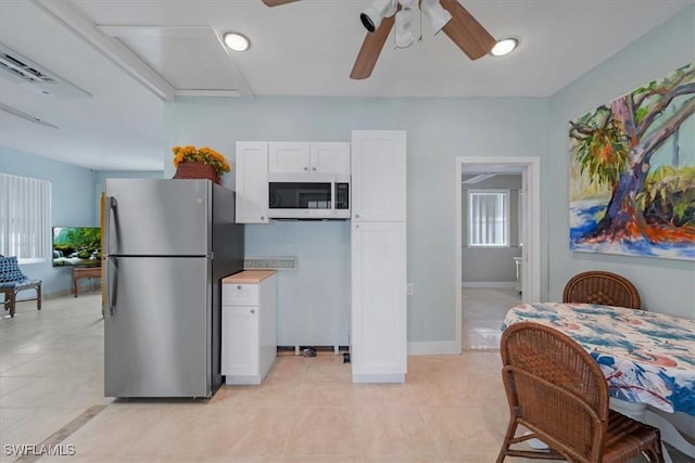 kitchen featuring light tile patterned floors, white microwave, freestanding refrigerator, white cabinetry, and baseboards