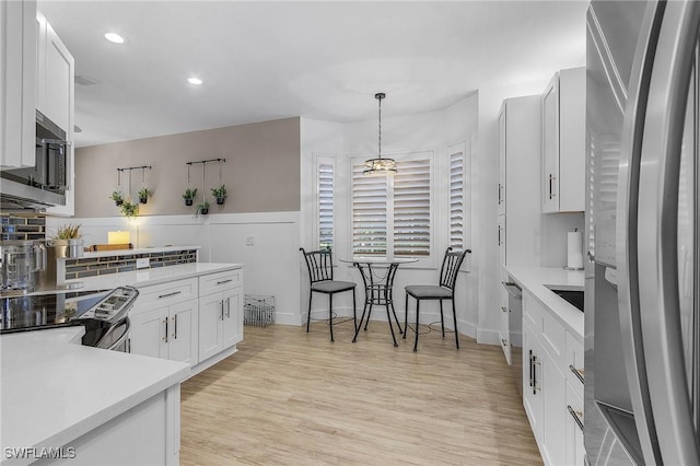 kitchen with stainless steel appliances, pendant lighting, white cabinets, and light hardwood / wood-style flooring