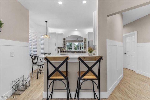 kitchen featuring decorative light fixtures, white cabinetry, a breakfast bar area, kitchen peninsula, and light hardwood / wood-style flooring