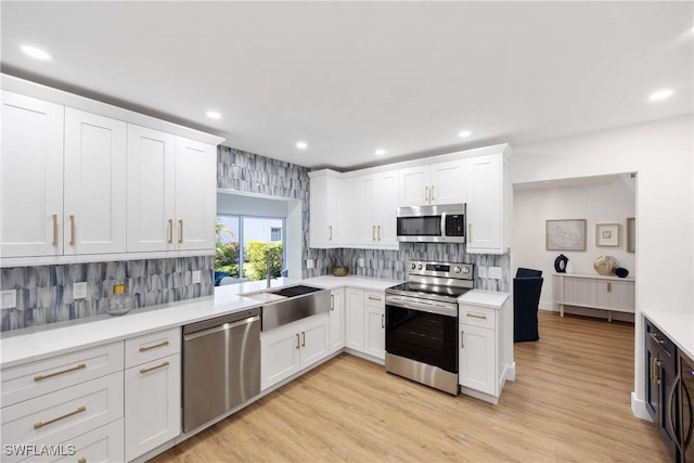 kitchen with stainless steel appliances, sink, white cabinets, and light wood-type flooring