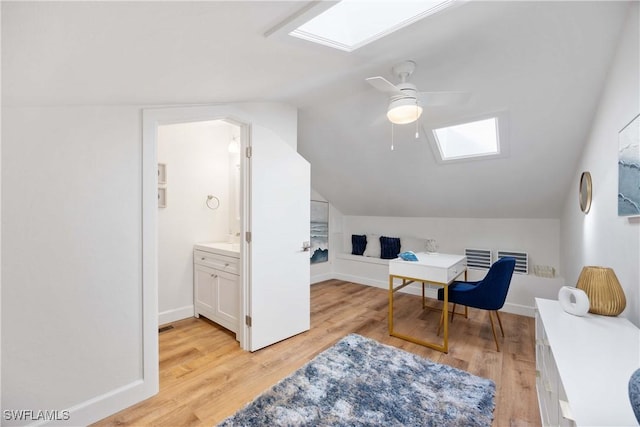 home office with ceiling fan, vaulted ceiling with skylight, and light wood-type flooring