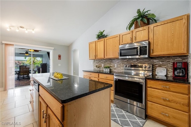 kitchen with lofted ceiling, appliances with stainless steel finishes, a center island, light tile patterned flooring, and decorative backsplash