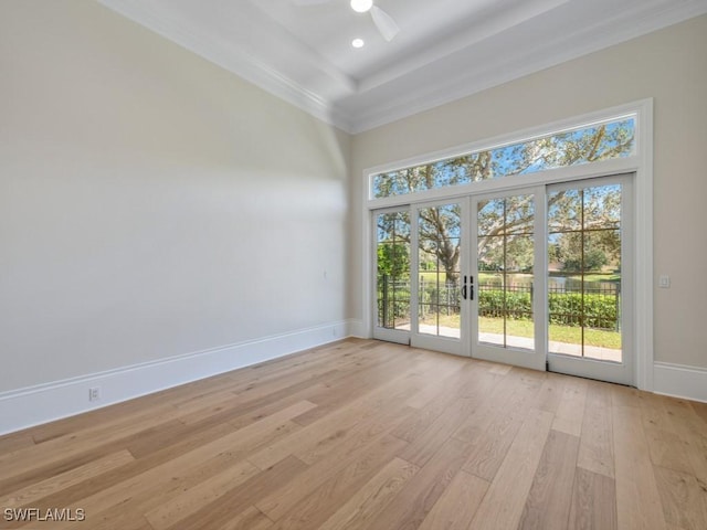 spare room with a raised ceiling, a wealth of natural light, light wood-type flooring, and french doors