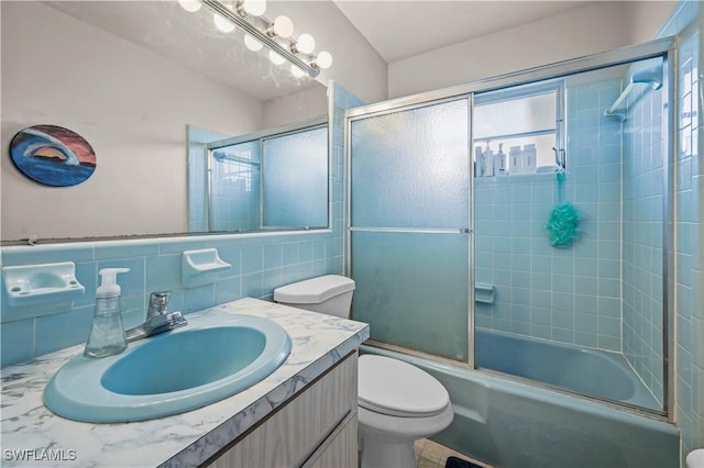 full bathroom featuring vanity, tile walls, shower / bath combination with glass door, and toilet