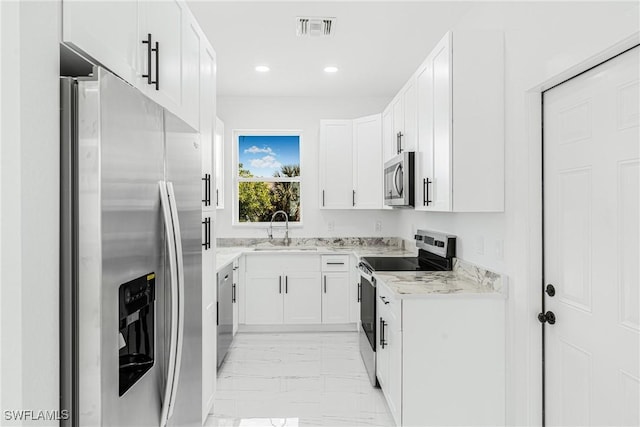 kitchen featuring white cabinetry, stainless steel appliances, light stone countertops, and sink