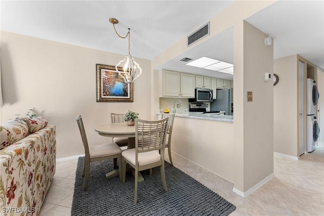 dining room featuring an inviting chandelier, light tile patterned floors, sink, and stacked washer and clothes dryer