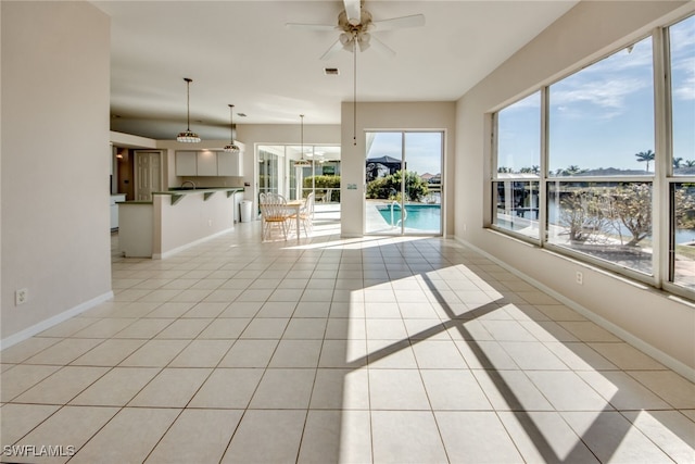 interior space with a water view, ceiling fan with notable chandelier, and light tile patterned floors