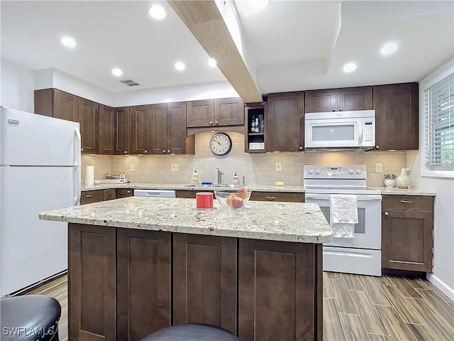 kitchen with dark brown cabinetry, tasteful backsplash, light stone counters, and white appliances