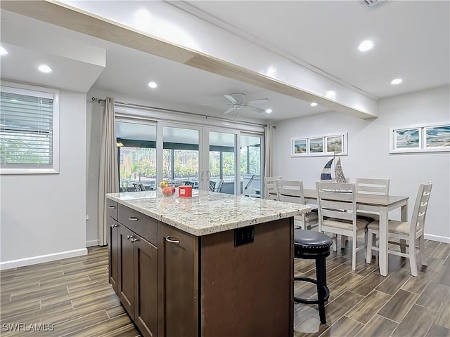 kitchen with a center island, ceiling fan, light stone counters, dark brown cabinets, and french doors