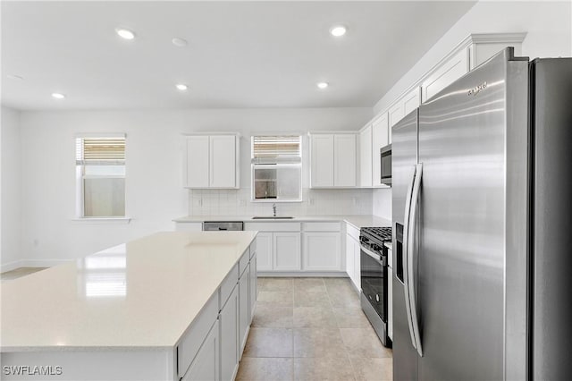 kitchen featuring sink, appliances with stainless steel finishes, a center island, white cabinets, and decorative backsplash