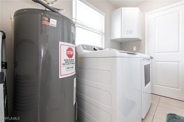 clothes washing area featuring water heater, washer and dryer, light tile patterned floors, and cabinets