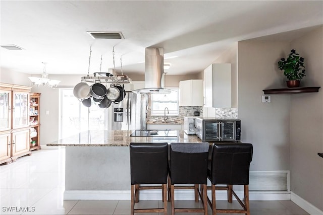 kitchen featuring tasteful backsplash, white cabinetry, island exhaust hood, stainless steel refrigerator with ice dispenser, and light stone countertops