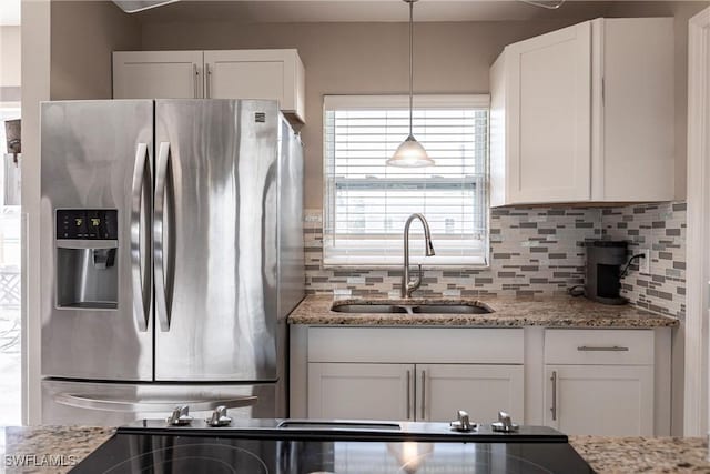 kitchen with tasteful backsplash, white cabinetry, sink, stainless steel fridge, and light stone countertops